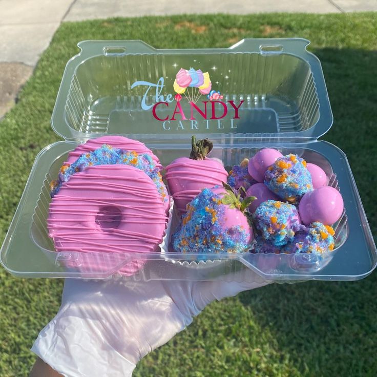 there is a plastic container with pink and blue frosted donuts in it on the grass