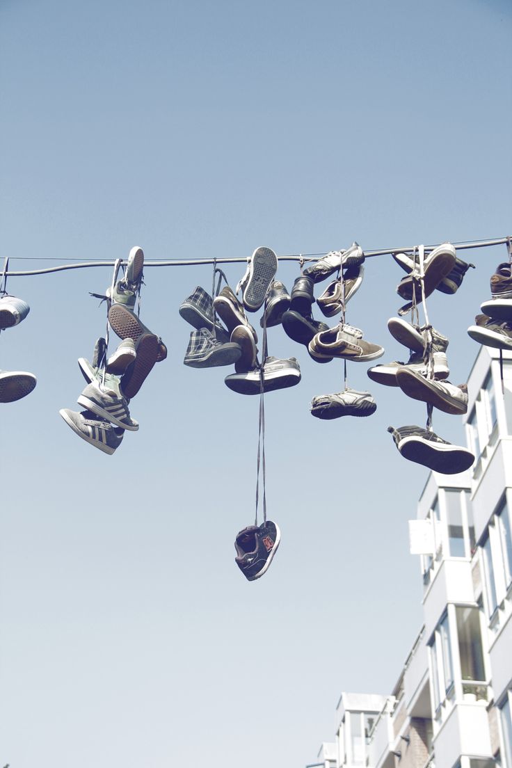 several pairs of shoes hanging on a clothes line in front of a tall building with apartment buildings