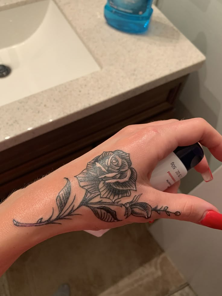 a woman's hand with a rose tattoo on it holding an empty roll of deodorant