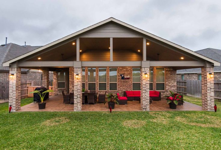 a covered patio with red couches and potted plants on the grass in front of it