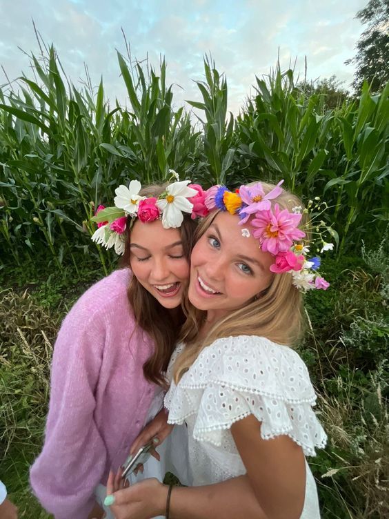 two girls with flower crowns on their heads are posing for the camera in front of cornfield