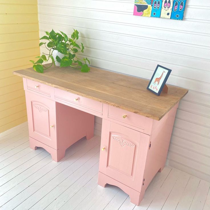 a pink desk with a potted plant sitting on it's top, in front of a white wall