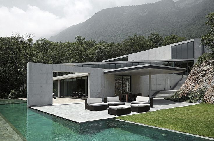 a house with a pool in front of it and some mountains behind the house that is surrounded by grass