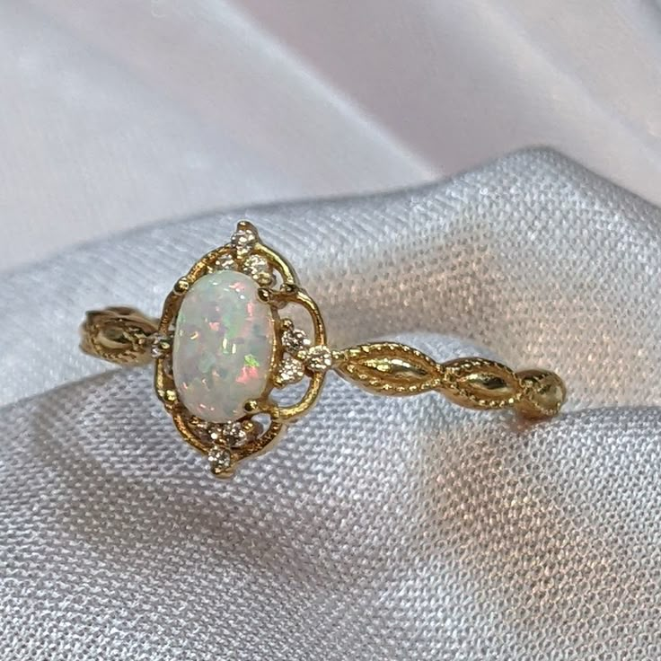 an opal and diamond ring is sitting on a white piece of cloth with gold trimmings