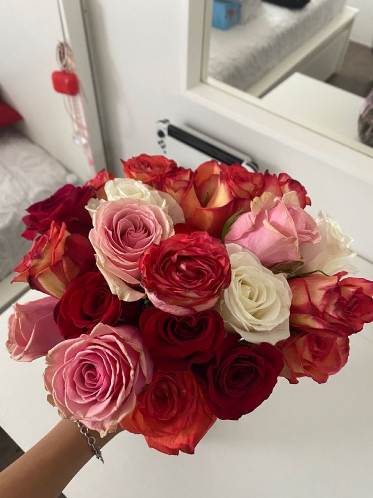 a person holding a bouquet of red and white flowers in front of a bedroom mirror