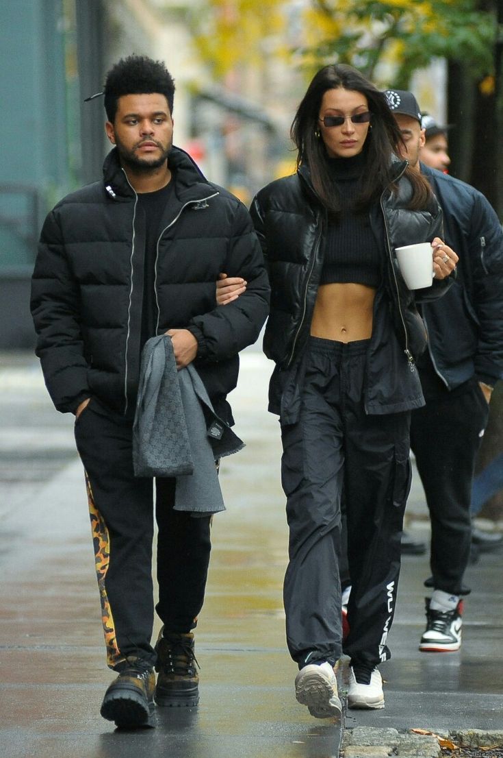 two people walking down the street with one holding a coffee cup in her hand and another carrying an umbrella