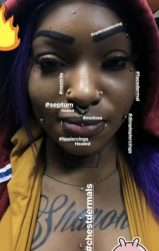 a woman with purple hair and piercings on her face has words written all over her face