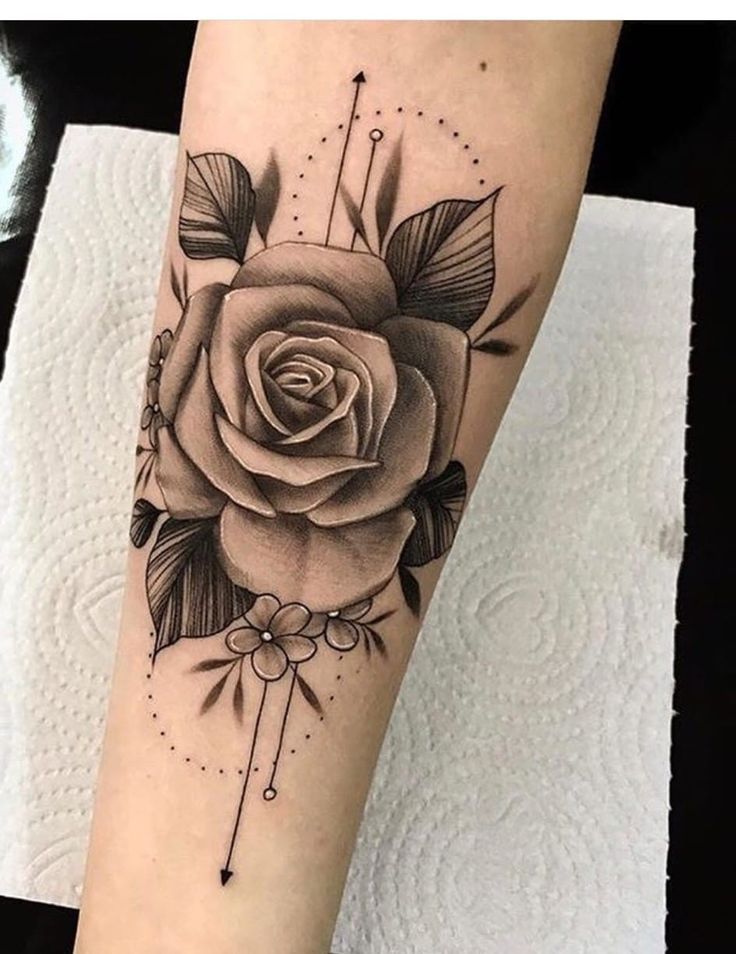 a black and white rose tattoo on the right forearm, with arrows around it's center