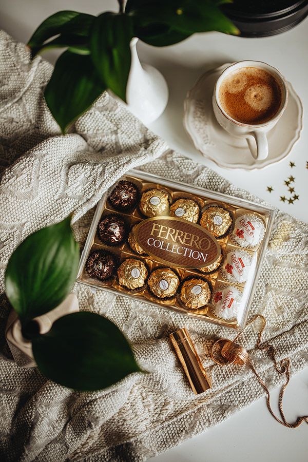 a box of chocolates next to a cup of coffee on a white tablecloth