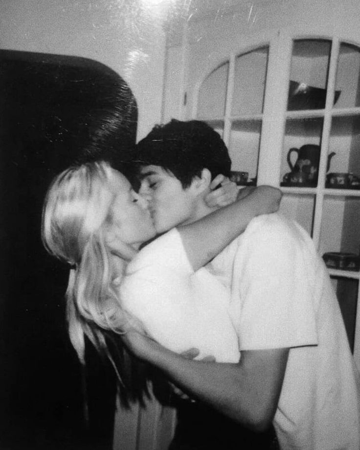 black and white photograph of a man kissing a woman's face in front of a bookshelf