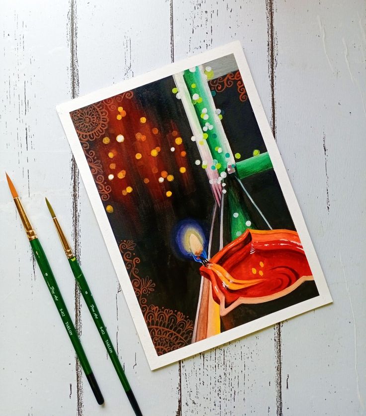 some paint brushes are laying next to an art print on a white wooden surface with two different colored pencils