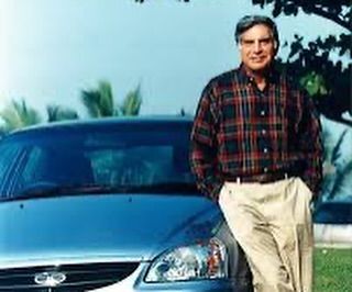 a man standing next to a blue car in front of a tree and grass area