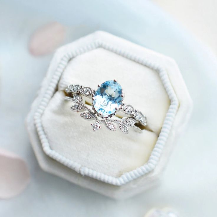 an engagement ring with a blue topaz sits in a white box on a table