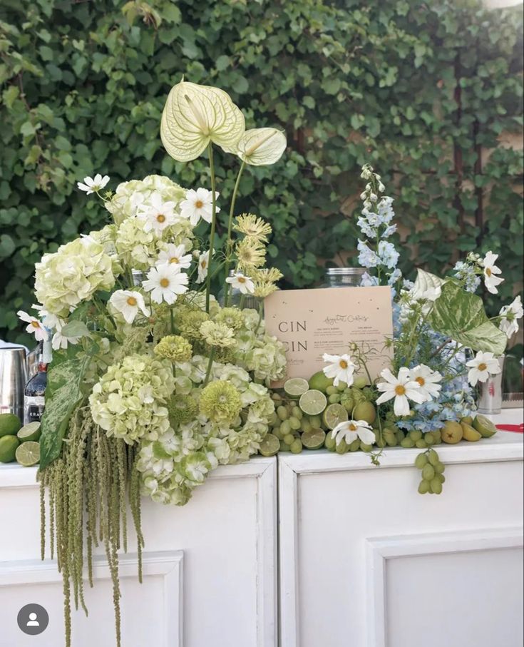 an arrangement of flowers and greenery on top of a cabinet