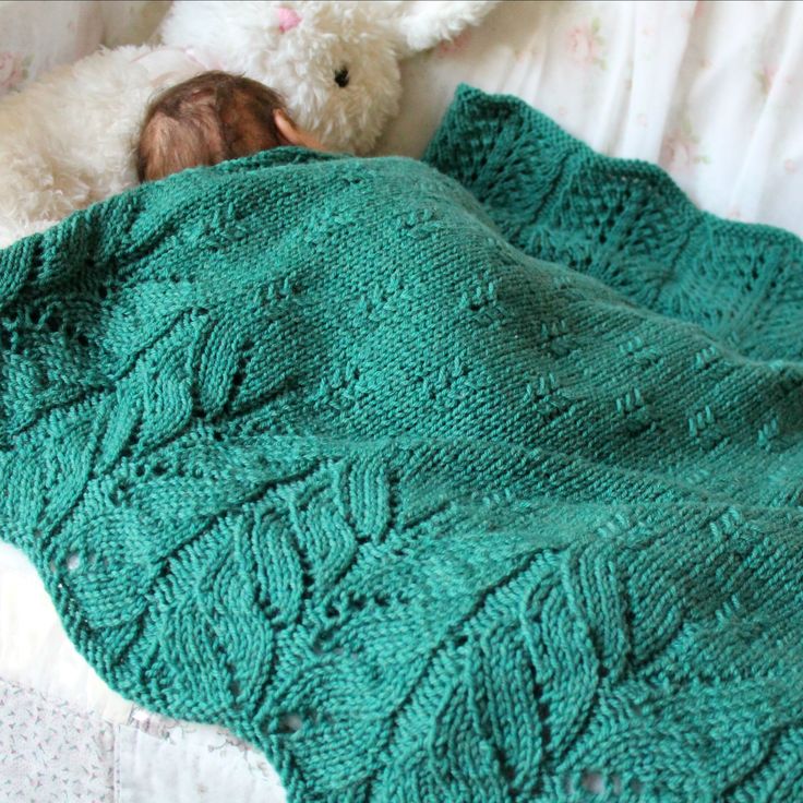 a baby wrapped in a green blanket next to a teddy bear on a white bed