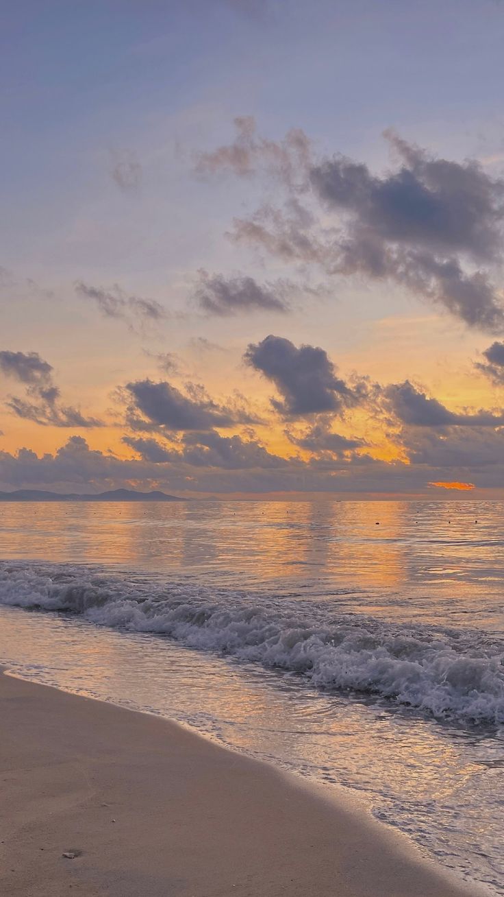 the sun is setting over the ocean with waves crashing on the shore and clouds in the sky