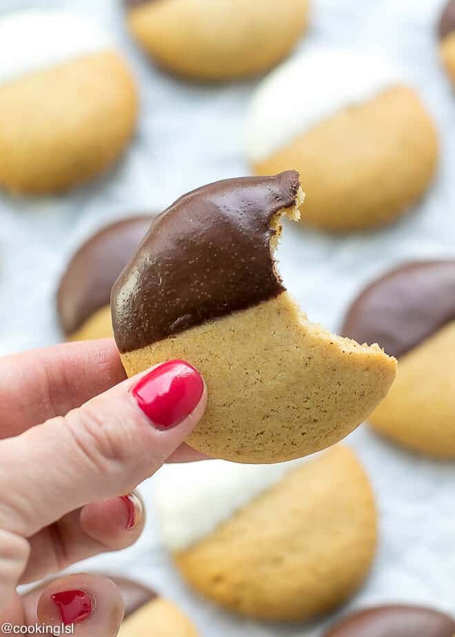 a half eaten chocolate covered cookie being held by a woman's hand with other cookies in the background