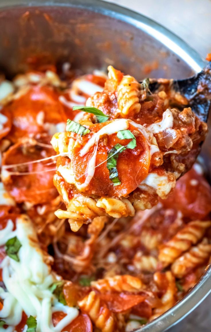 a spoon full of pasta with tomato sauce and parmesan cheese is being held up