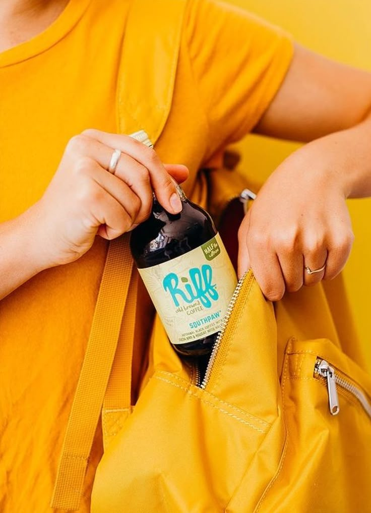 a person holding onto a yellow bag with a bottle in it's pocket,