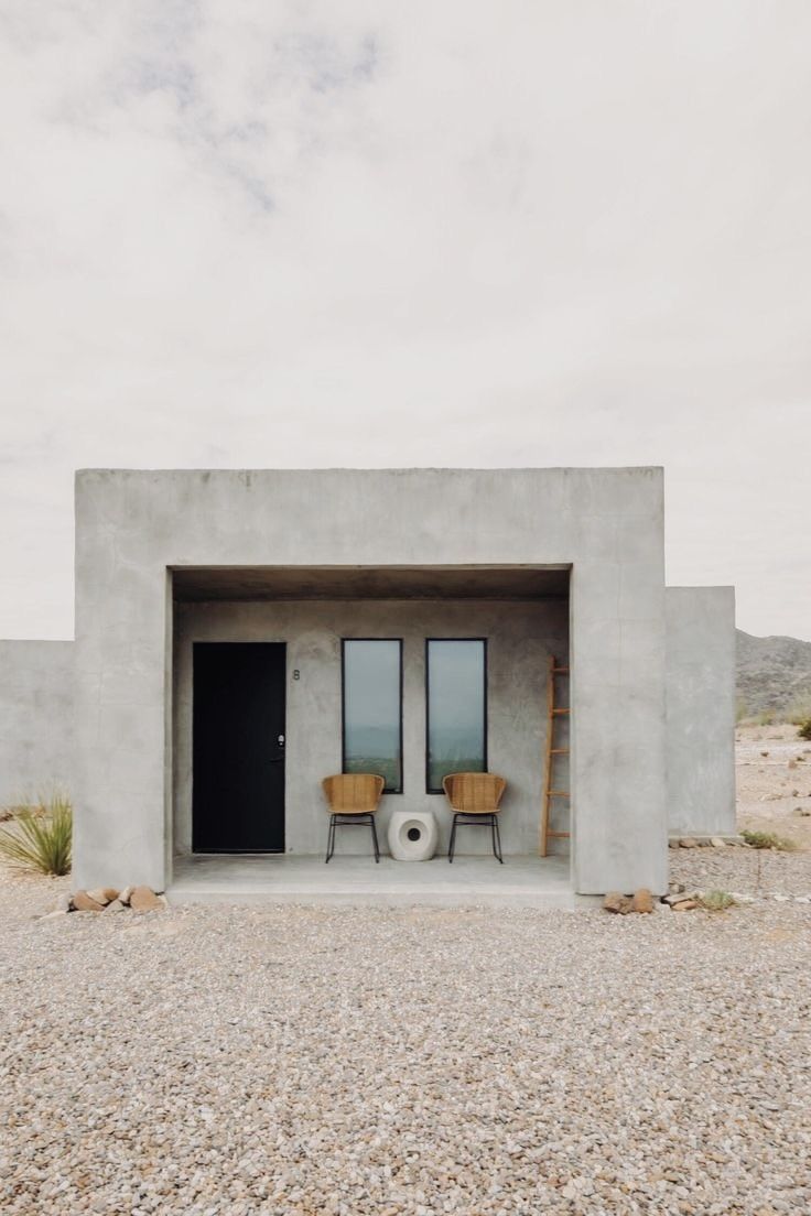 two chairs sitting in front of a concrete structure with doors and windows on the side