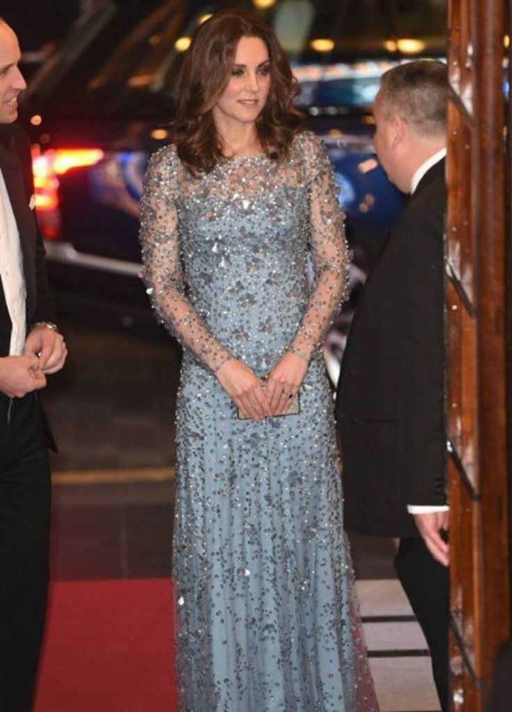 a woman in a long blue dress standing on a red carpet next to a man