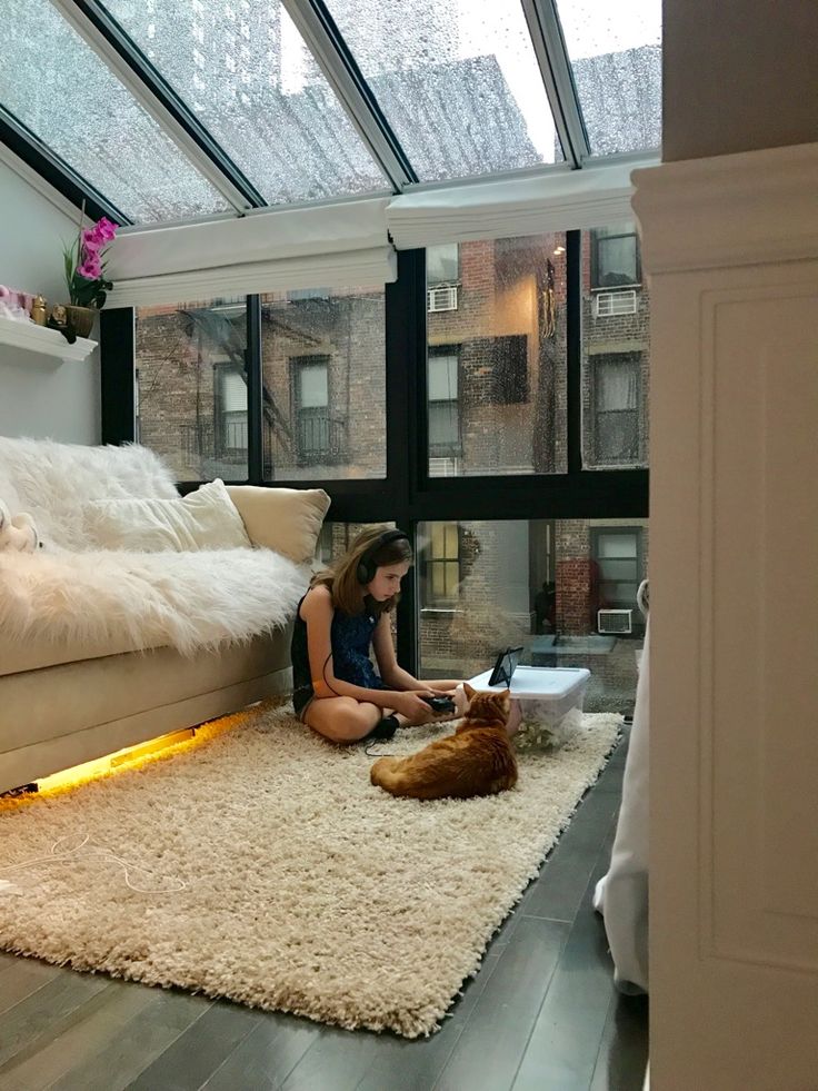 a woman sitting on the floor in front of a window with a dog laying next to her