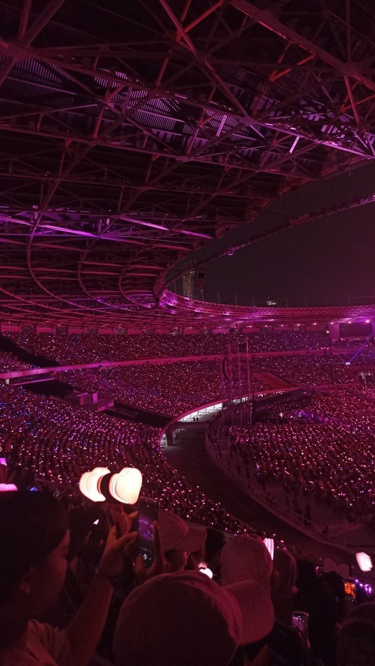 a large crowd at a concert with lights on and people in the audience taking pictures