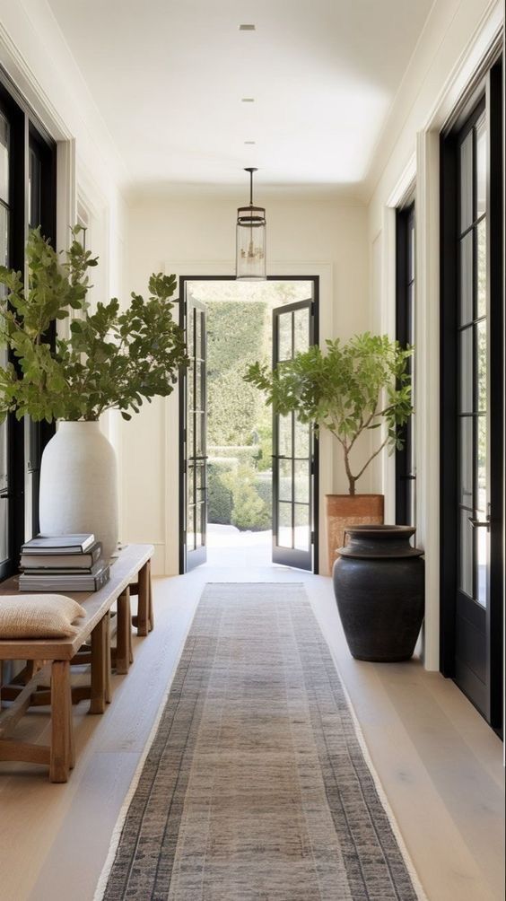 a long hallway with black and white doors and plants in vases on either side