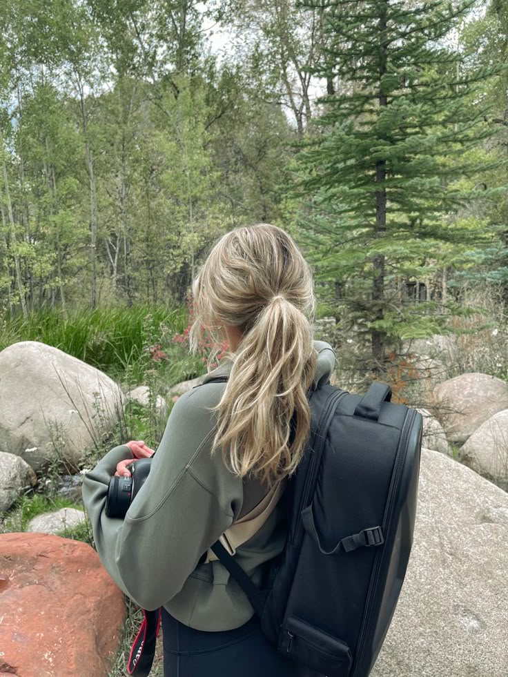 a woman standing on top of a large rock next to a forest filled with trees