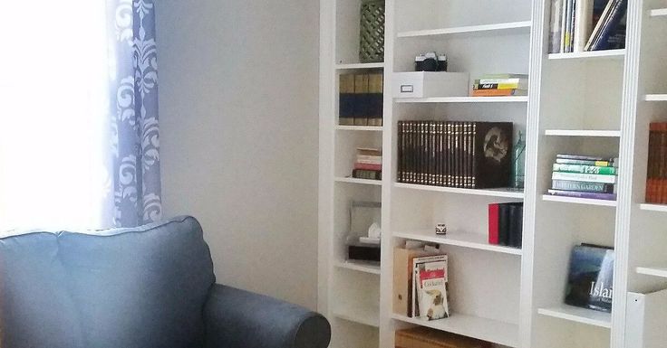 a living room filled with lots of white bookshelves next to a blue chair