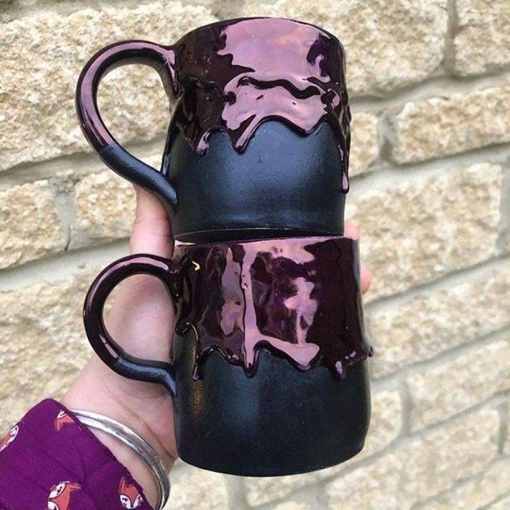 a hand holding a black and purple coffee mug with pink glaze on the outside