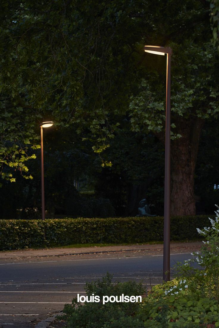 an empty street at night with two lamps on each side and trees in the background