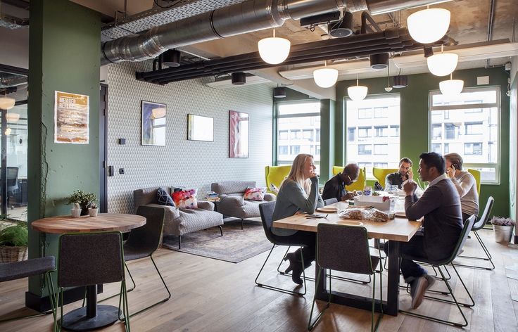 people are sitting at a table in an office with green walls and wood flooring