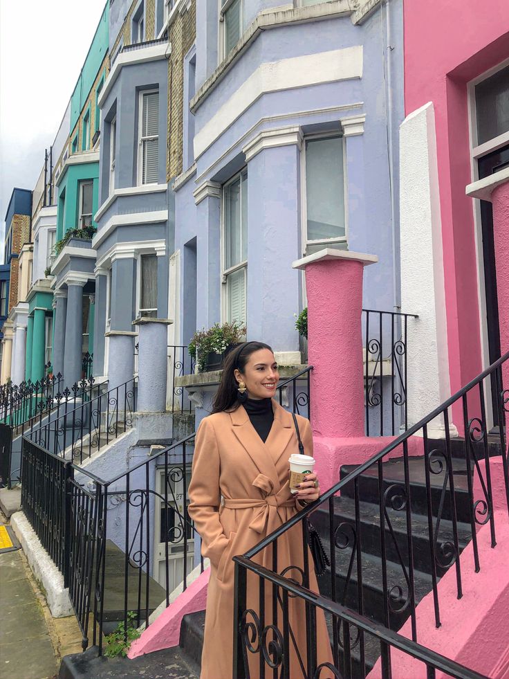 a woman is standing on the stairs in front of some colorful buildings and holding a cup