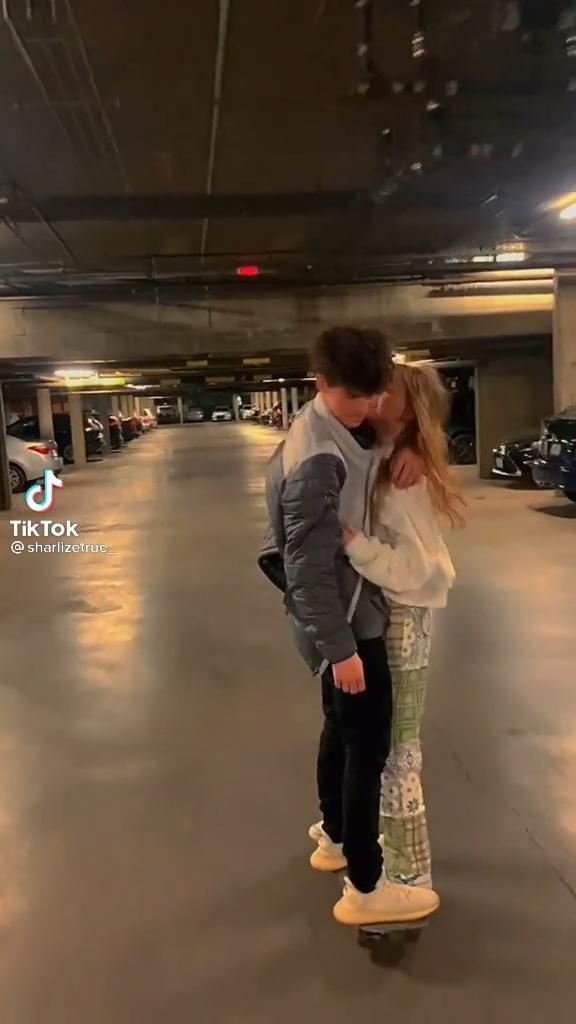 a man and woman are kissing in an empty parking garage with their skateboards on the ground