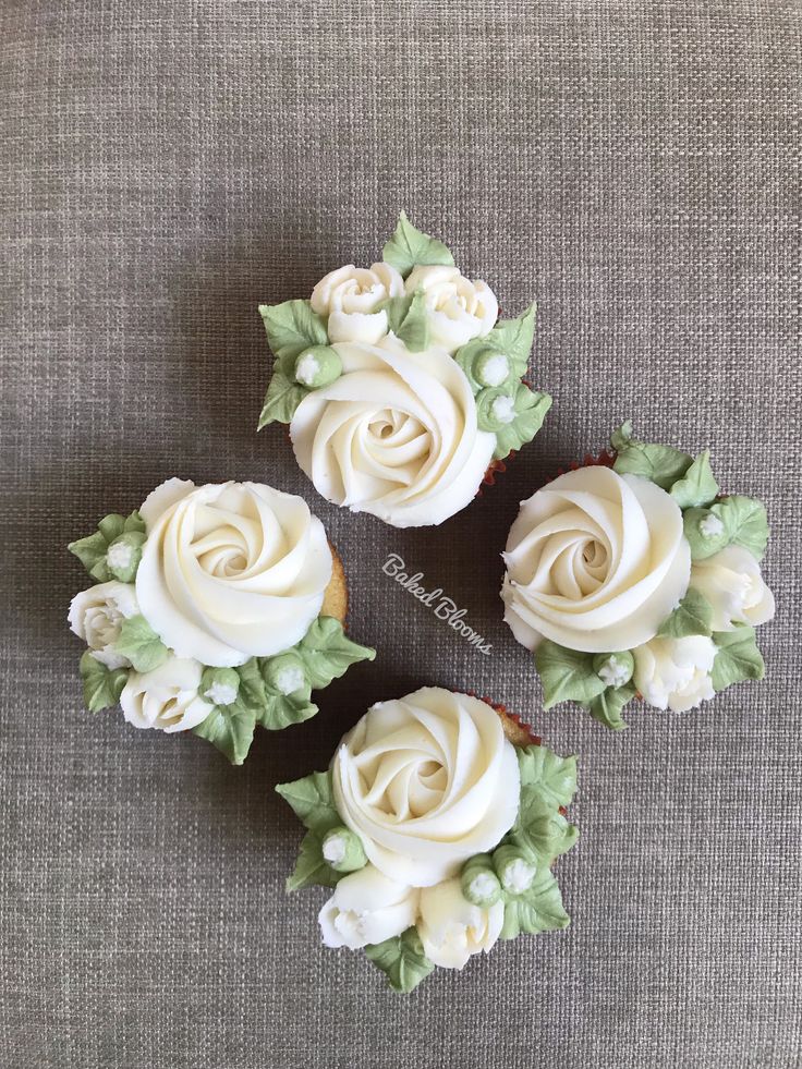 three cupcakes with white frosting and green leaves on top are arranged in the shape of roses