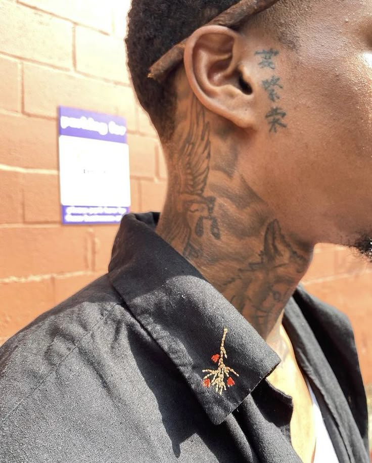 a man with tattoos standing in front of a brick wall and looking off to the side