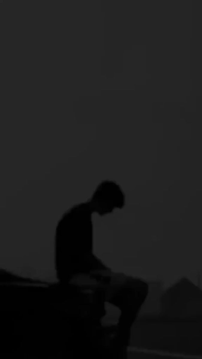 a man sitting on top of a bench in the dark with his hands behind him