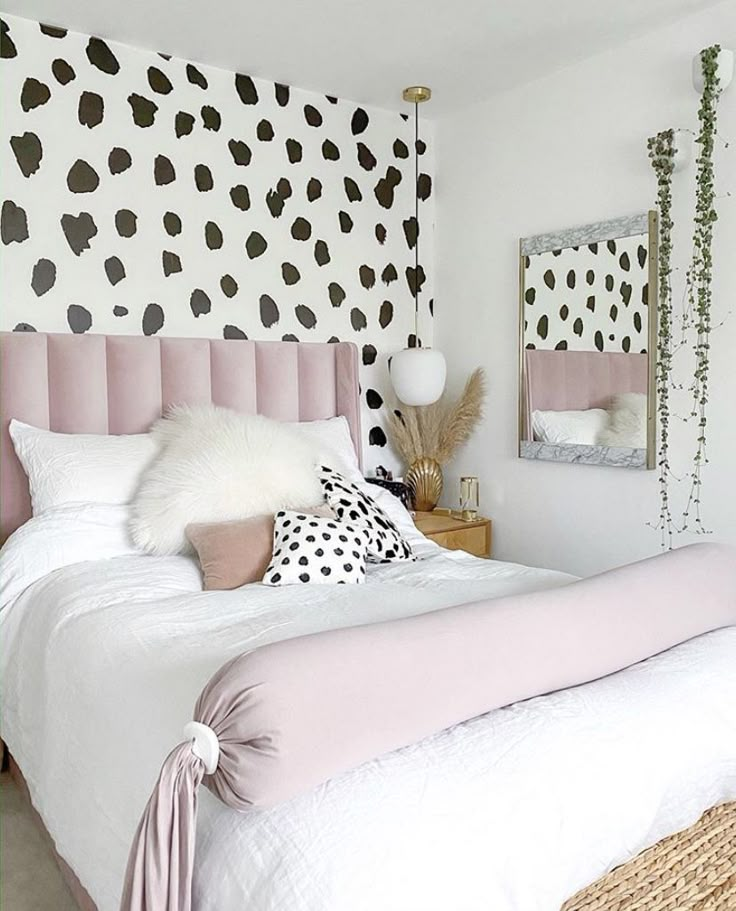 a white bed with pink and black pillows in a room decorated with polka dot wallpaper