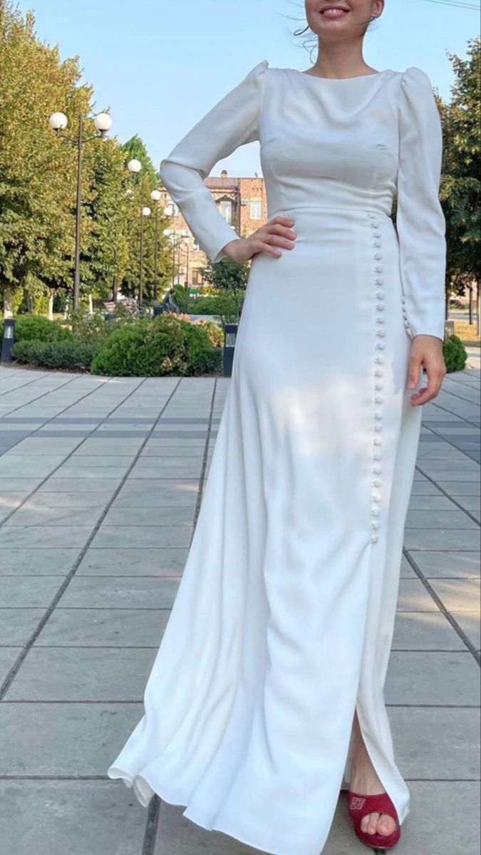 a woman in a long white dress standing on the sidewalk with her hands on her hips