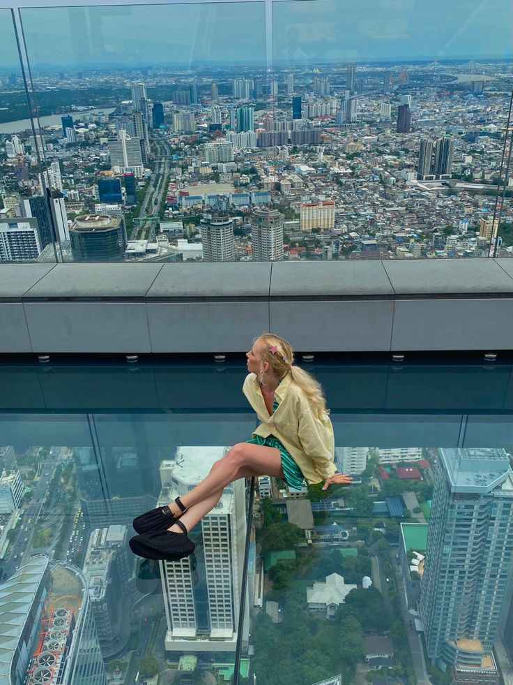 a woman sitting on top of a glass floor in front of a cityscape