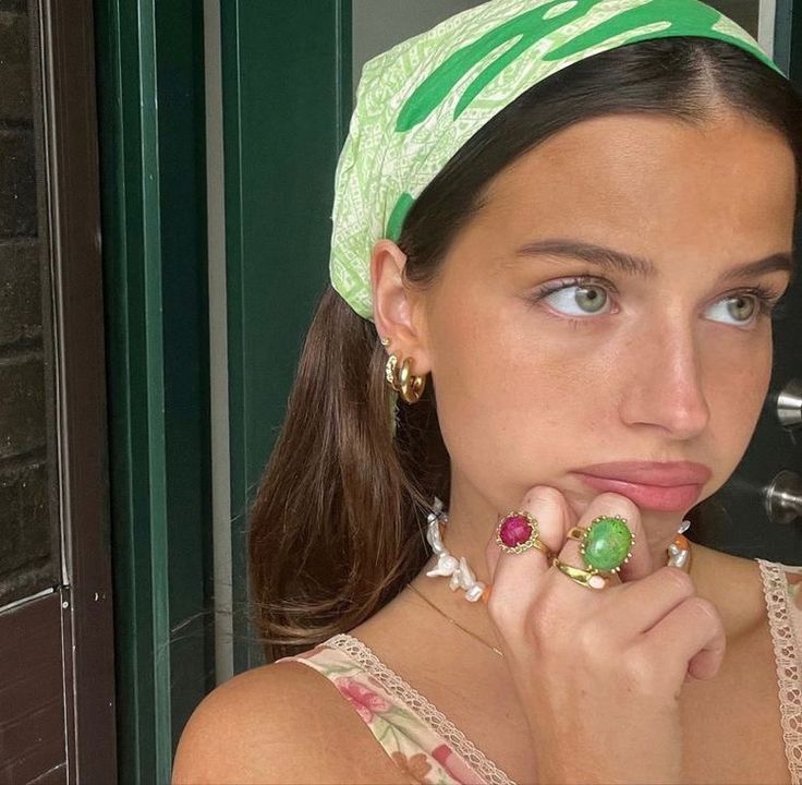 a woman wearing a green bandana and holding her finger to her mouth