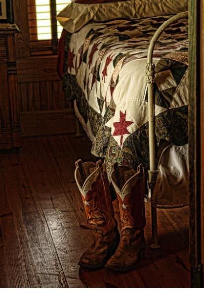 a pair of cowboy boots sitting on top of a wooden floor next to a bed