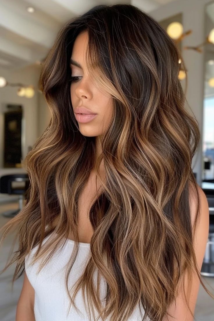 Woman with long, wavy, highlighted brown hair wearing a white tank top in a modern salon setting. Dark Root Caramel Balayage, Brunette With Brunette Highlights, Balayage Hair Blonde And Brown, Teasylights Dark Hair, Golden Balayage On Black Hair, Medium Brown Hair Balayage Caramel, Balayage For Wavy Hair, Hair Color With Dark Eyebrows, Multi Dimensional Brown Hair