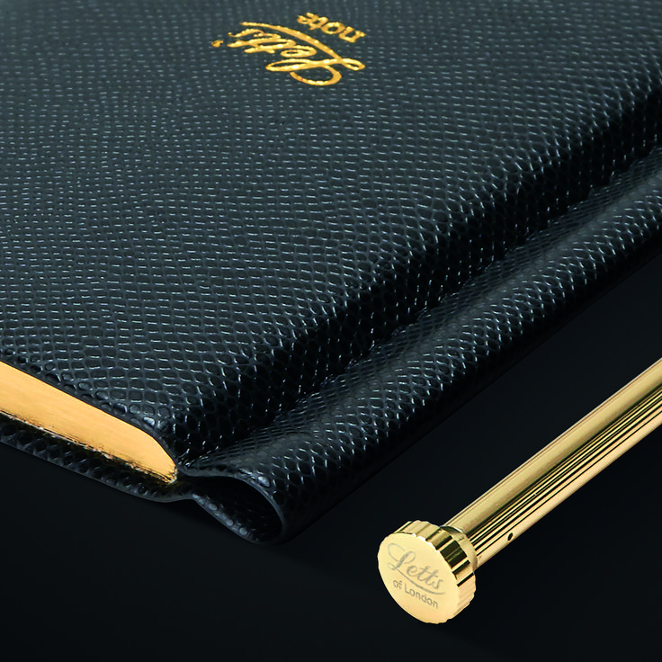 a pen is sitting on top of a black book with gold trimming and writing