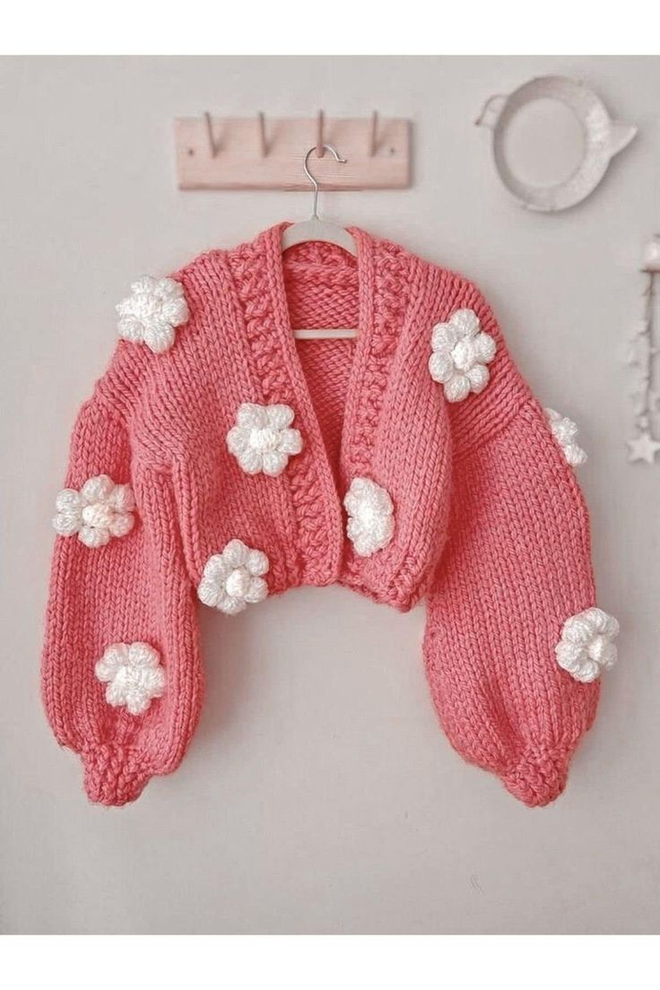 a pink knitted sweater with white flowers on it and a key hanging from the wall