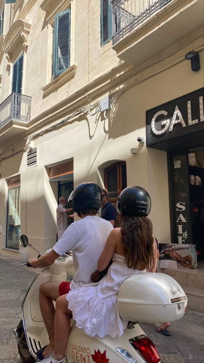 a man and woman riding on the back of a scooter down a street