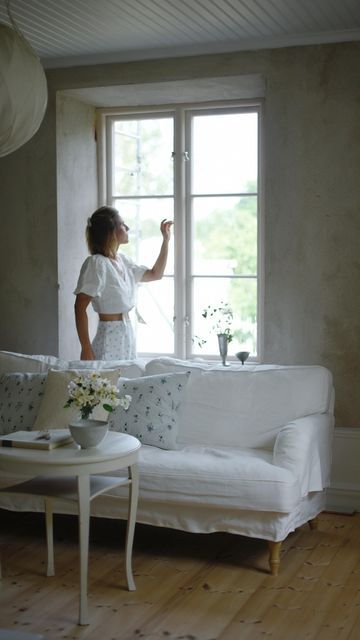 a woman standing in front of a window next to a white couch