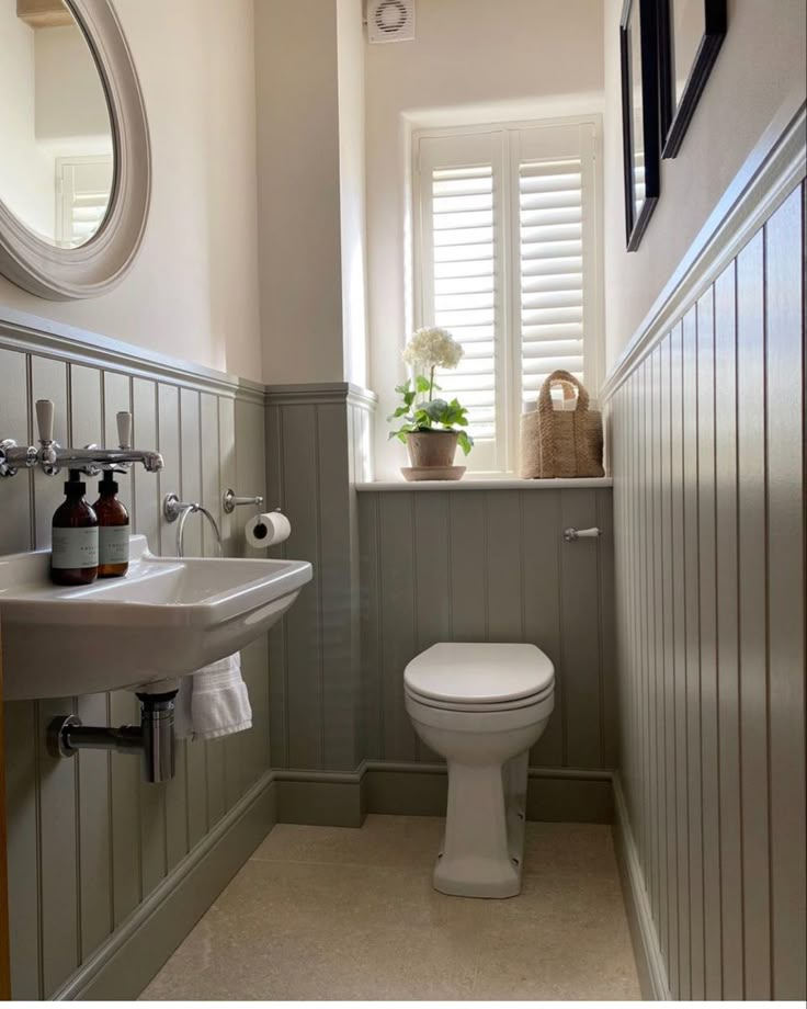 a white toilet sitting next to a sink in a bathroom under a window with shutters