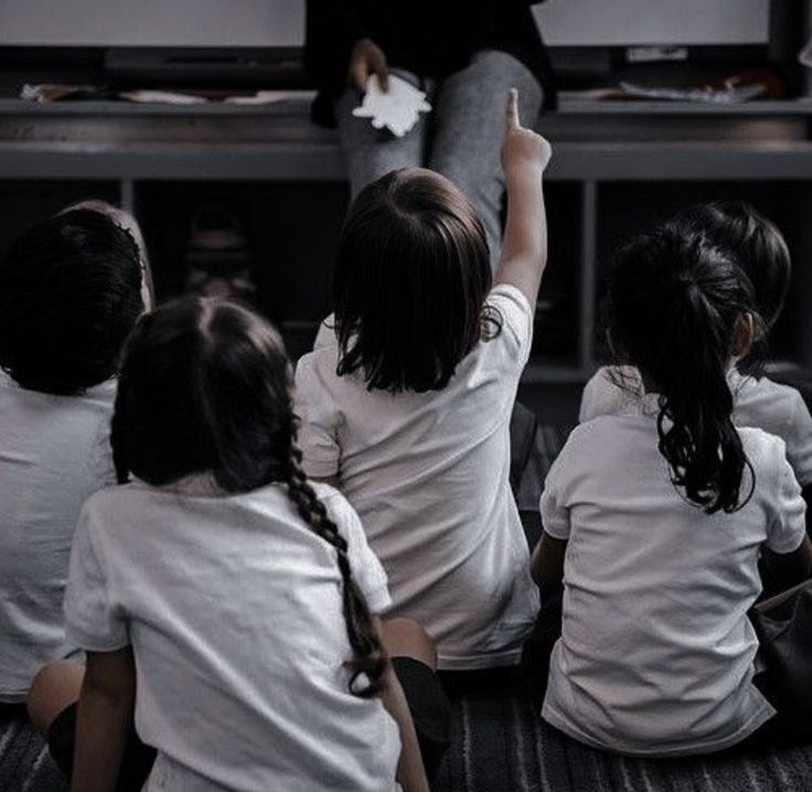 four children sitting on the floor watching television together and raising their hands in the air